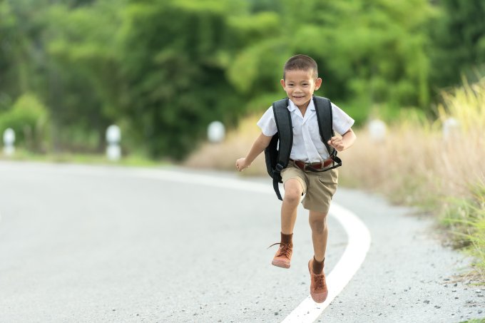 Chłopiec biegnie do szkoły z plecakiem na plecach